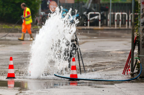 road spurt water beside traffic cones and a technician in backgr road spurt water beside traffic cones
