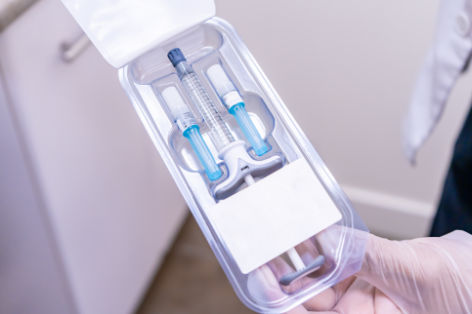 Doctor holding package of dermal filler with syringe vial and needles, for a softlift, non-surgical facelift with MD Codes on a medical cosmetic patient. Uses hyaluronic acid (HA) for anti-aging. Medical Packaging