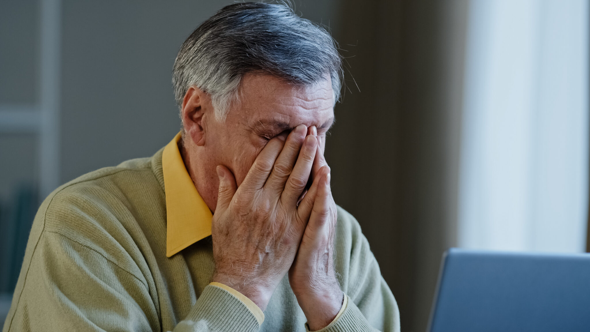 Older businessman with hands folded over his mouth and nose in frustration.