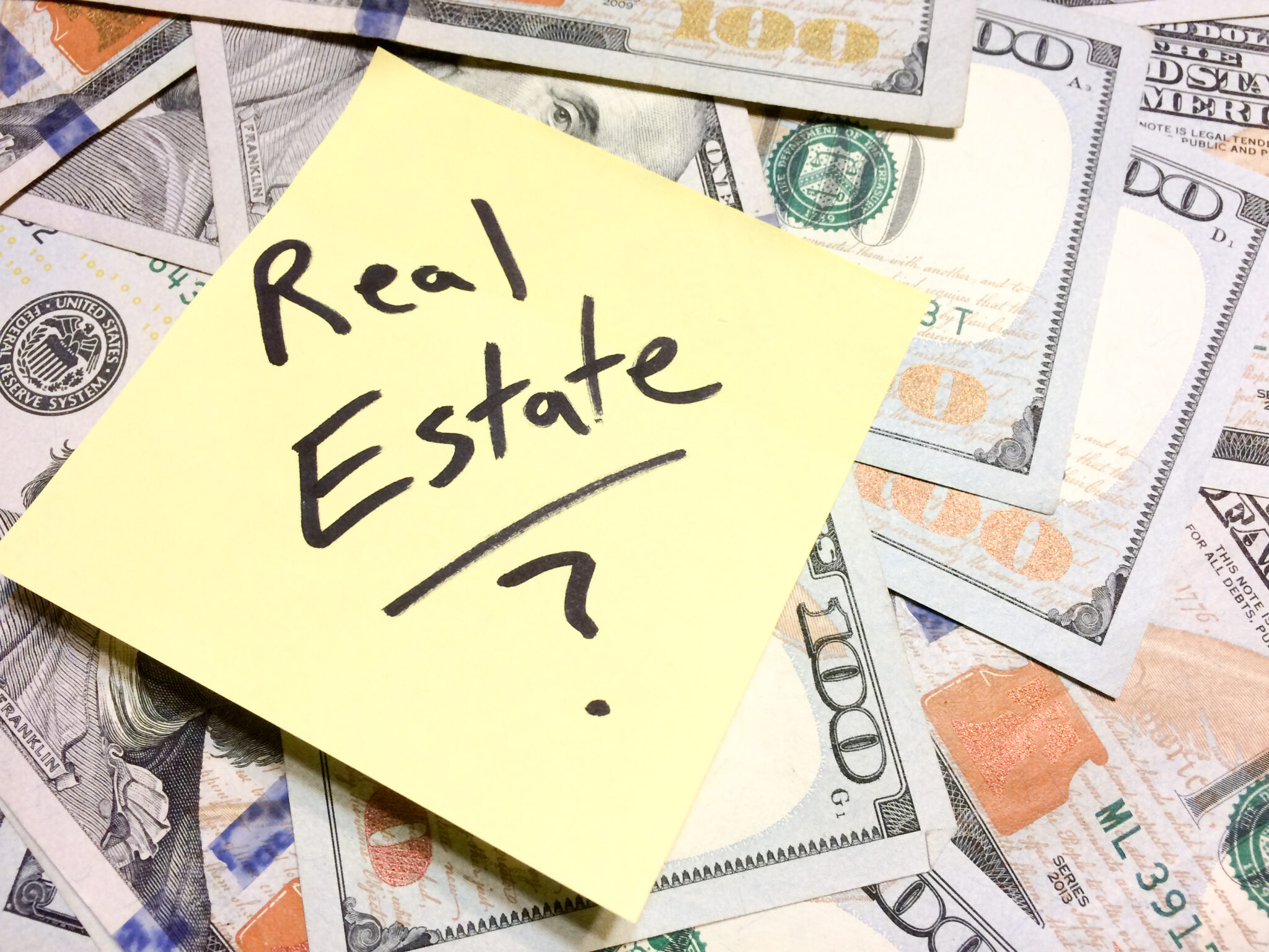 American cash money and yellow sticky note with text Real Estate question mark American cash money and yellow sticky note with text Real Estate with question mark in black color aerial view